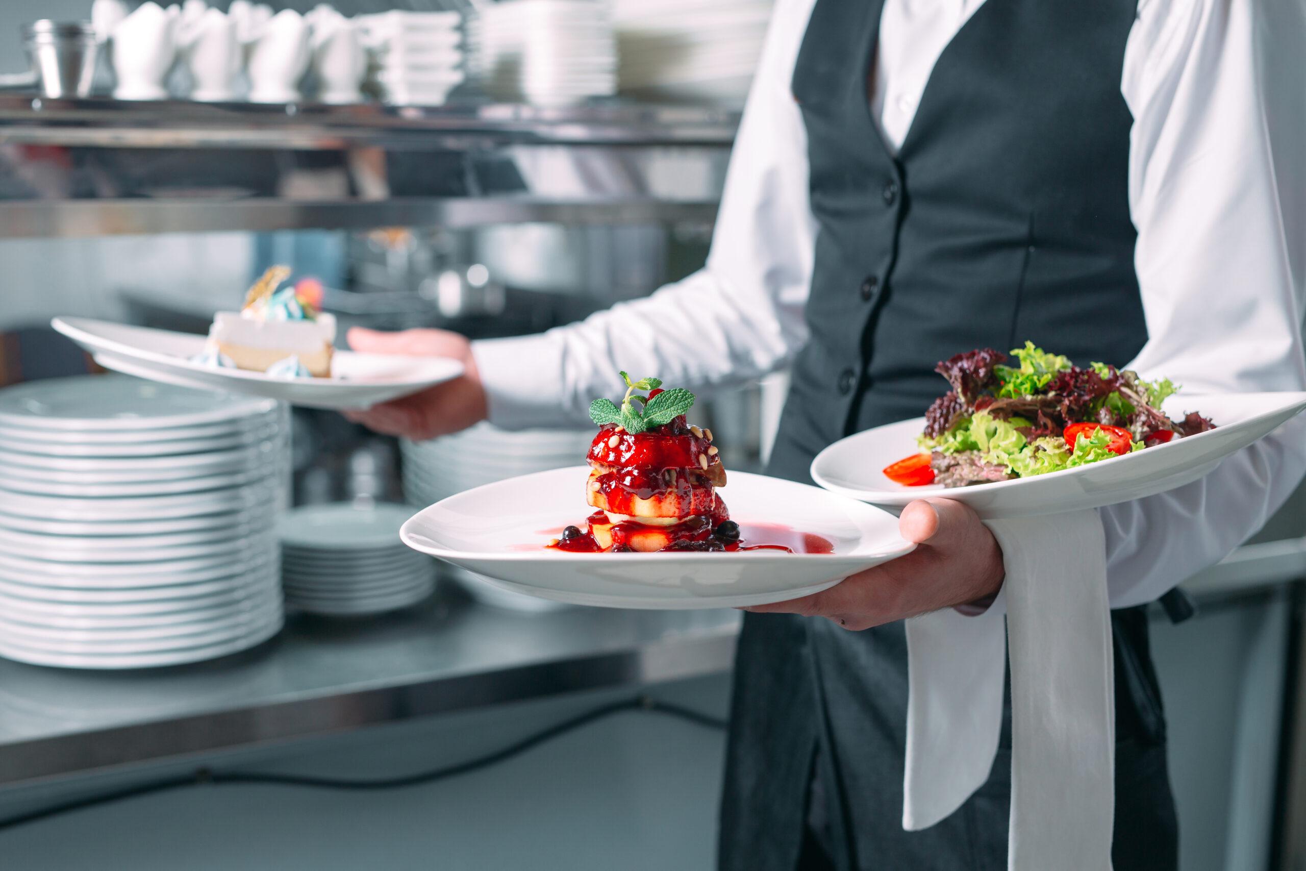 waiter in kitchen balancing plates of food on forearm and hands